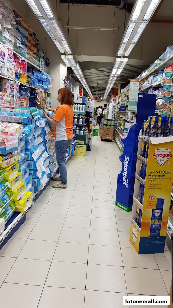A woman shops for products in a well-lit supermarket aisle with many shelves stocked.