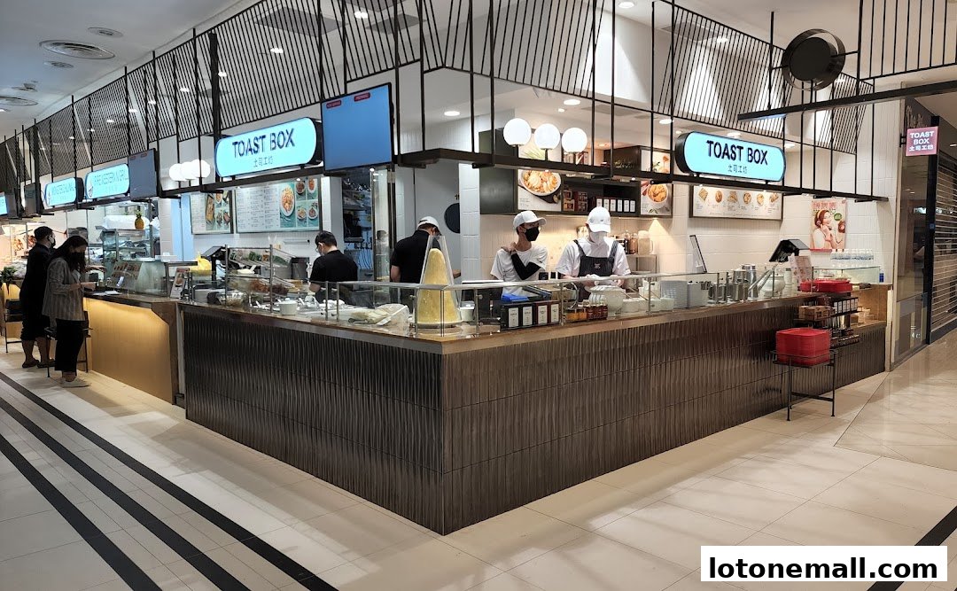 A food court counter with staff serving customers and various food displays.