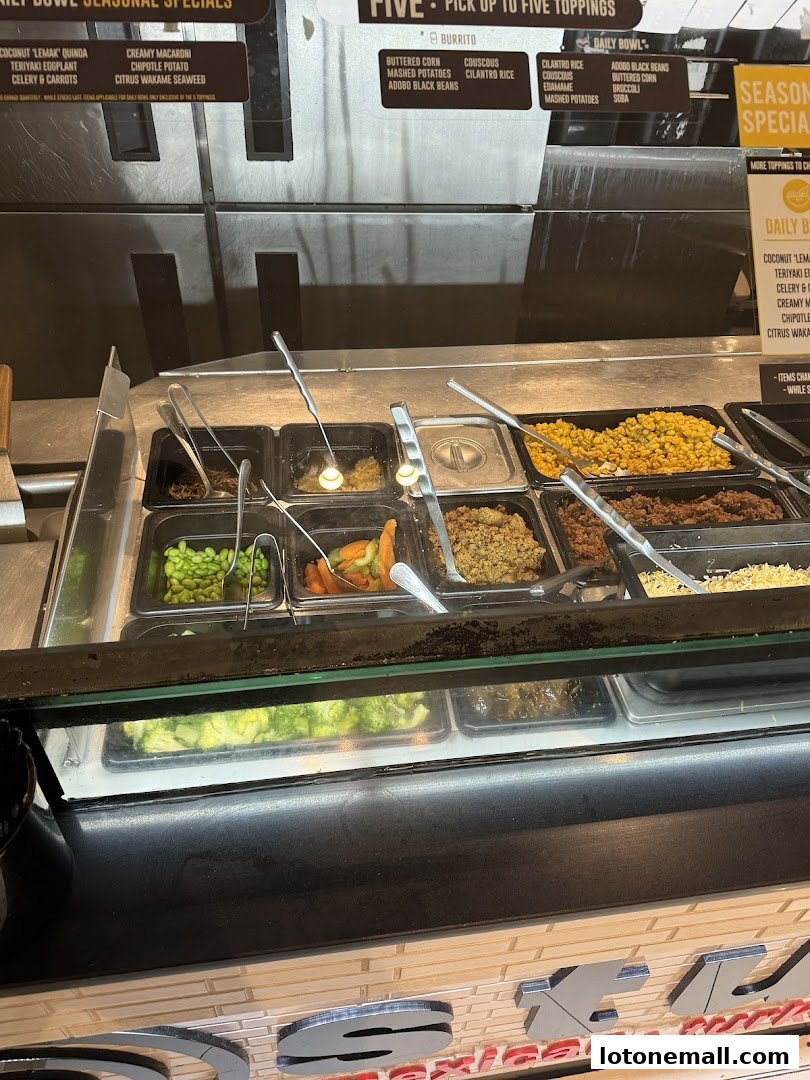 A display of fresh ingredients and toppings for bowls and burritos at a restaurant.
