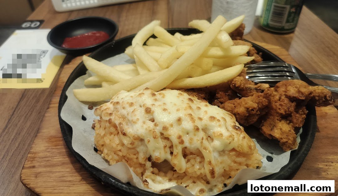 A sizzling plate of fried chicken, french fries, and cheesy rice with a side of ketchup.