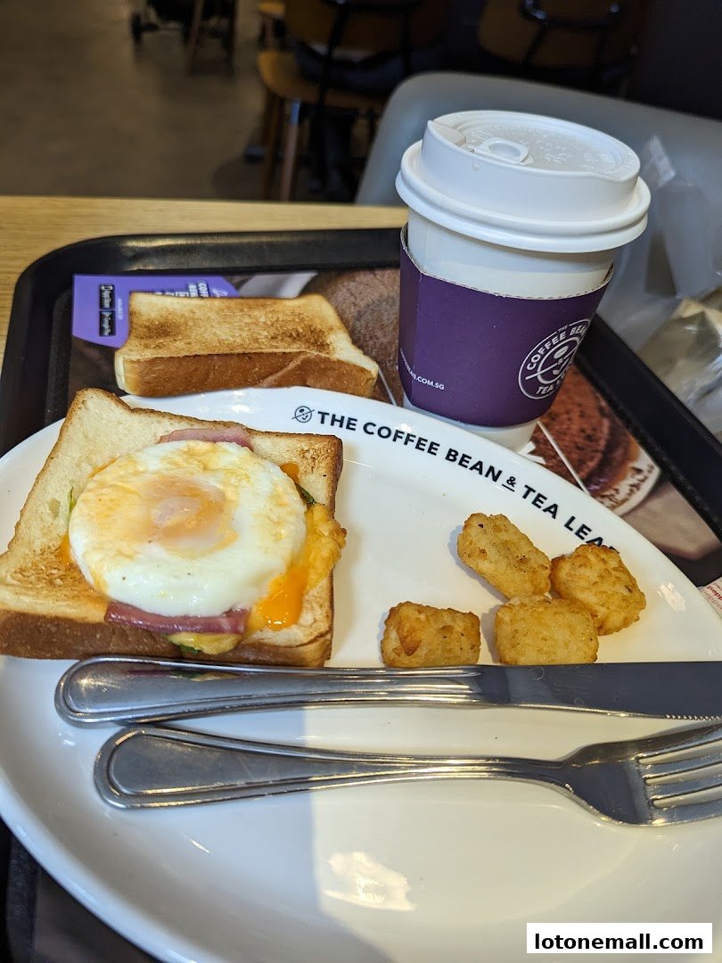 A breakfast meal with a sandwich, toast, tater tots, and a coffee cup on a tray.