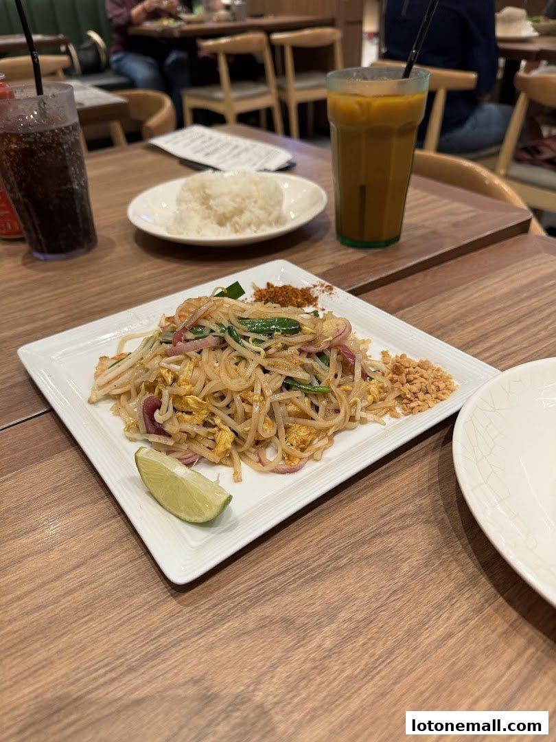 A plate of Pad Thai with a lime wedge and a drink on a wooden table.