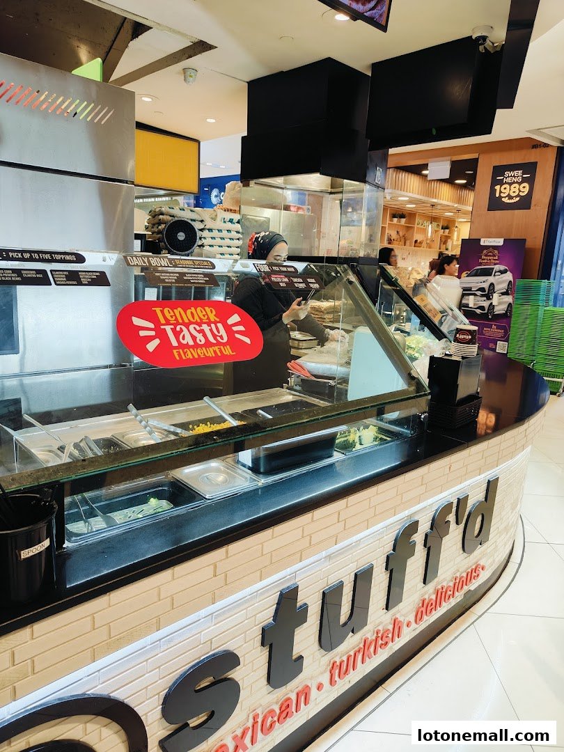 A food counter with various ingredients and a staff member preparing food.