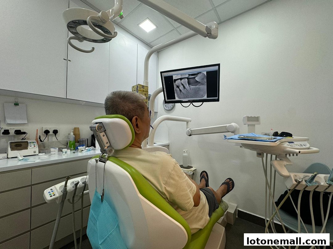 A patient sits in a dental chair while a dental X-ray is displayed on a monitor.