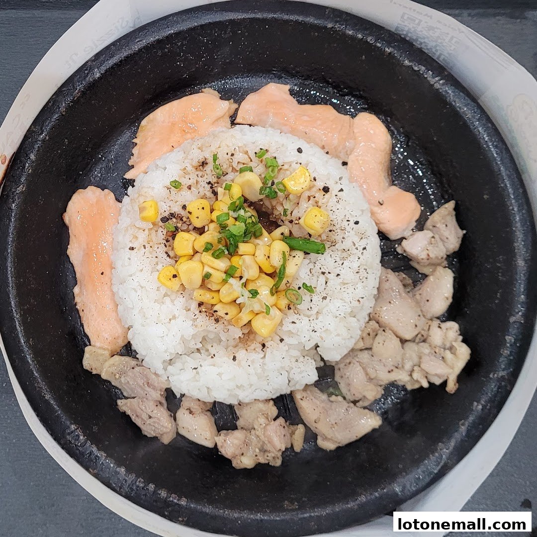 A sizzling hot plate with rice, corn, chicken, and salmon.