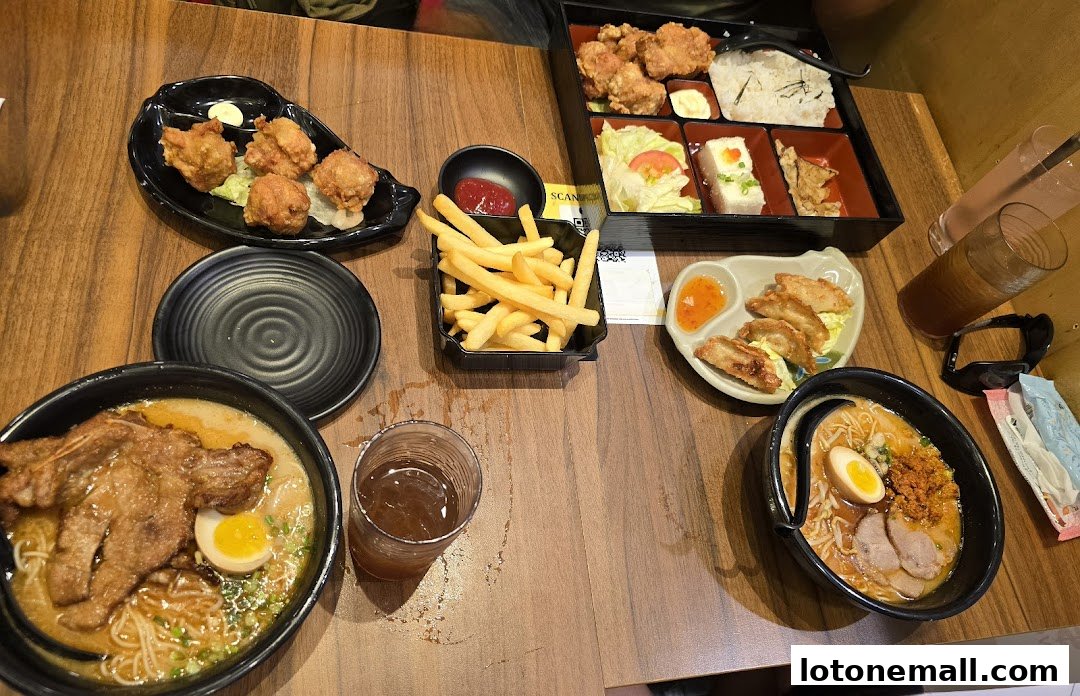 A table laden with various Japanese dishes including ramen, fried chicken, gyoza, fries, and drinks.