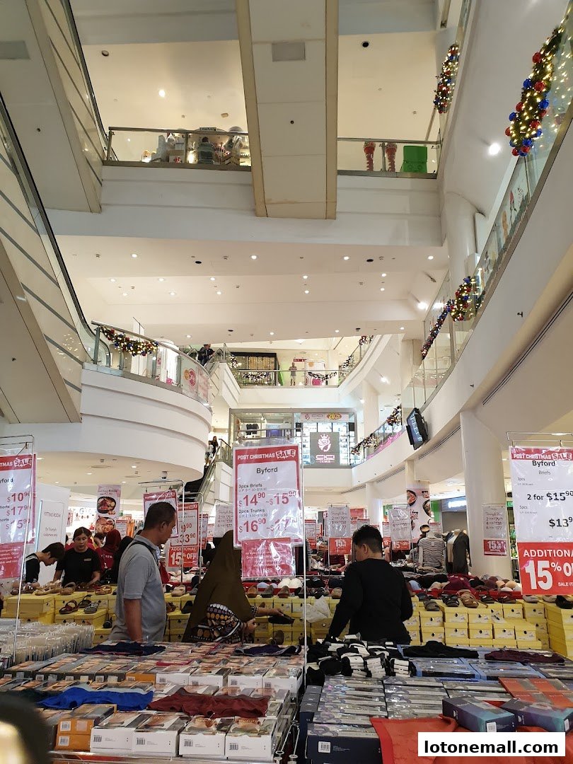 A busy shopping mall interior with Christmas decorations and a post-Christmas sale display.