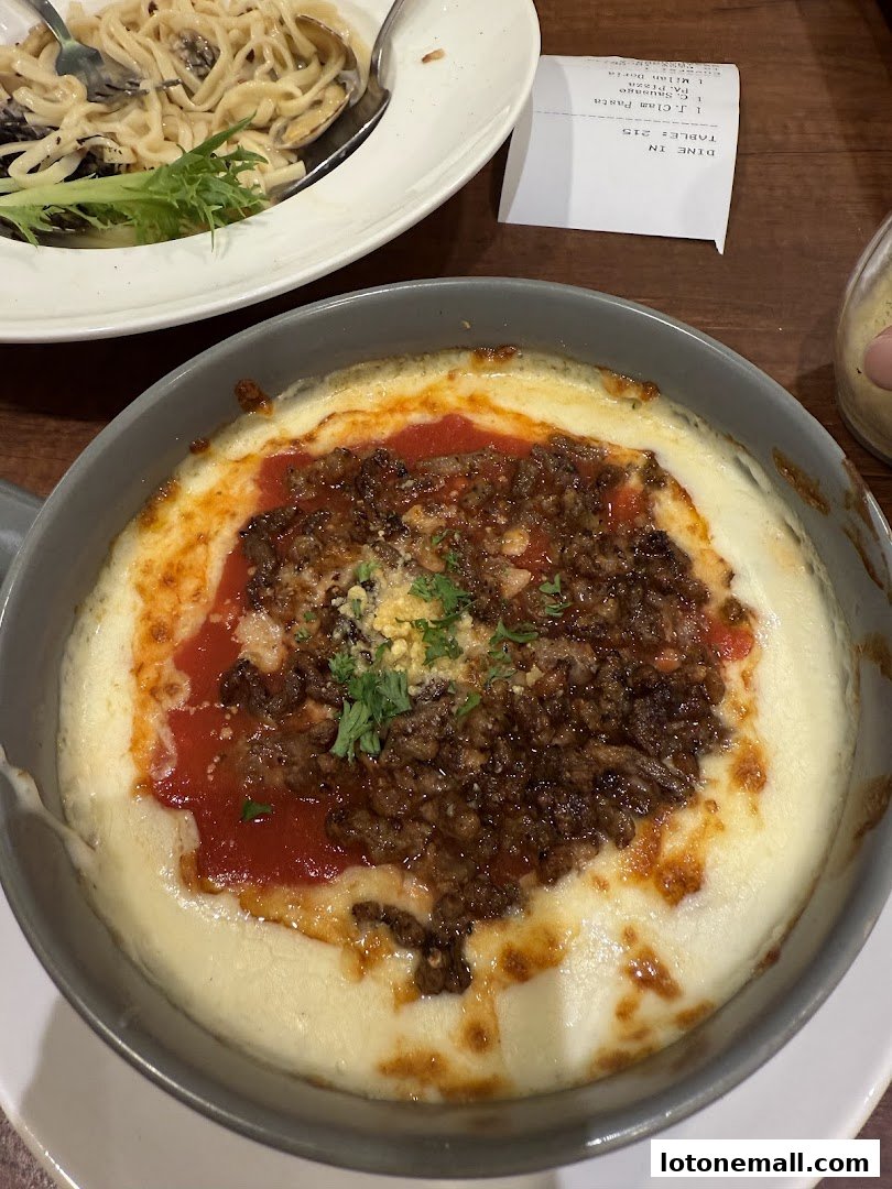 A close-up of a cheesy baked dish with meat sauce and a side of pasta.