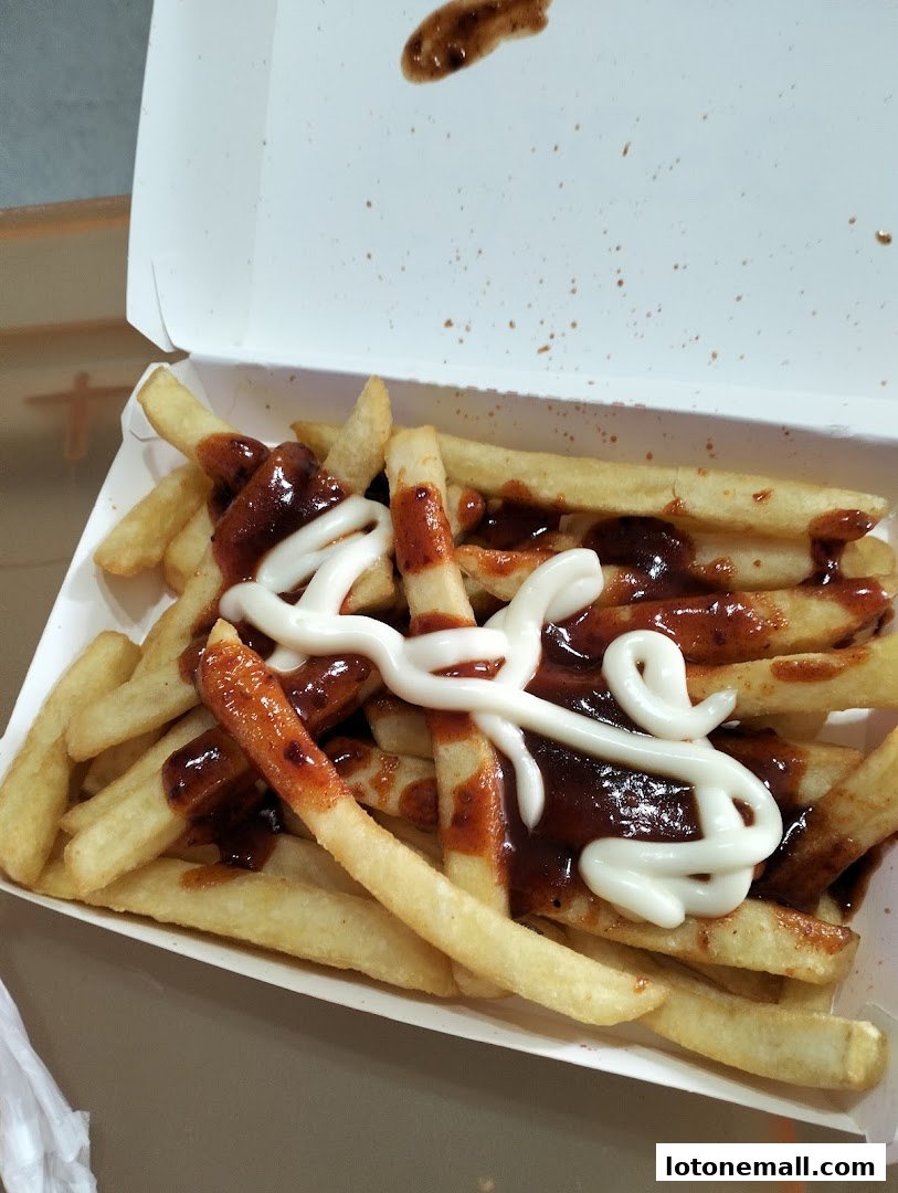 A box of golden french fries topped with barbecue sauce and mayonnaise.