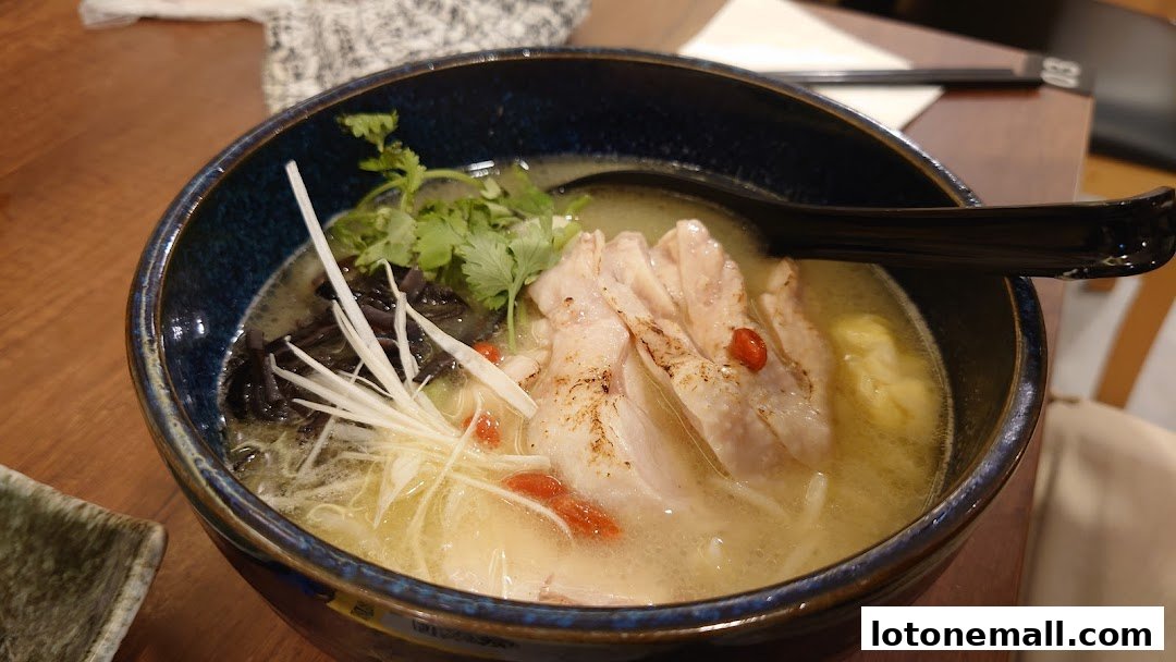 A close-up shot of a steaming bowl of ramen with tender chicken slices and fresh toppings.