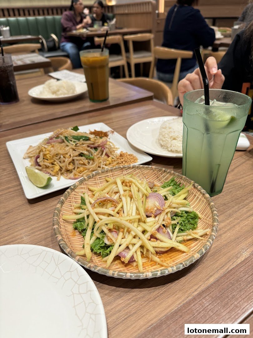 A table at Sanook Kitchen with Thai dishes and drinks, including Pad Thai and mango salad.