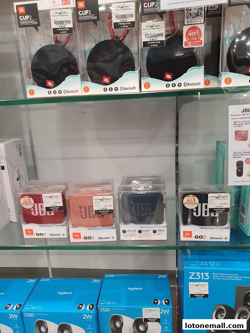 Shelves display various JBL portable Bluetooth speakers and Logitech speakers.