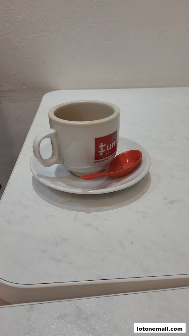 A white coffee cup and saucer with a red spoon on a marble table.