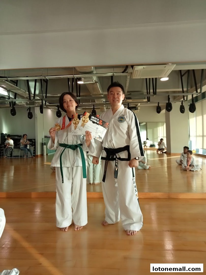 A Taekwondo instructor and student pose with medals and certificates.