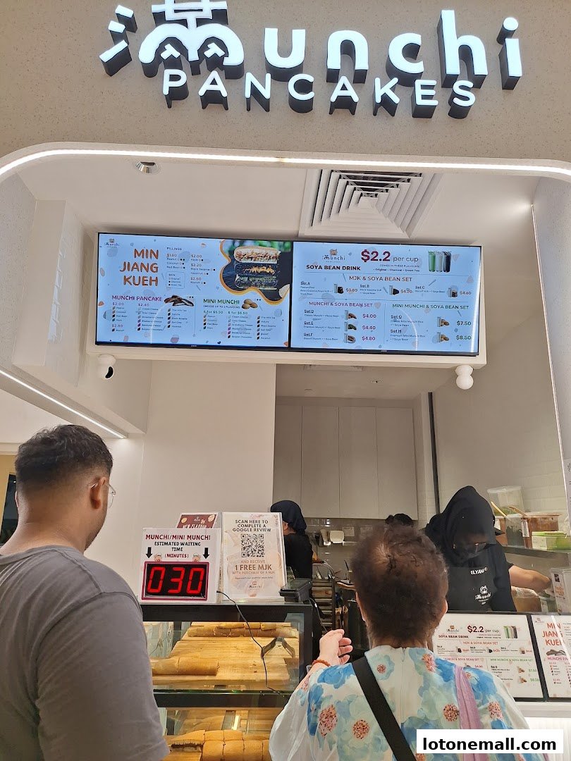 A digital menu board displays various pancake and drink options at Munchi Pancakes.