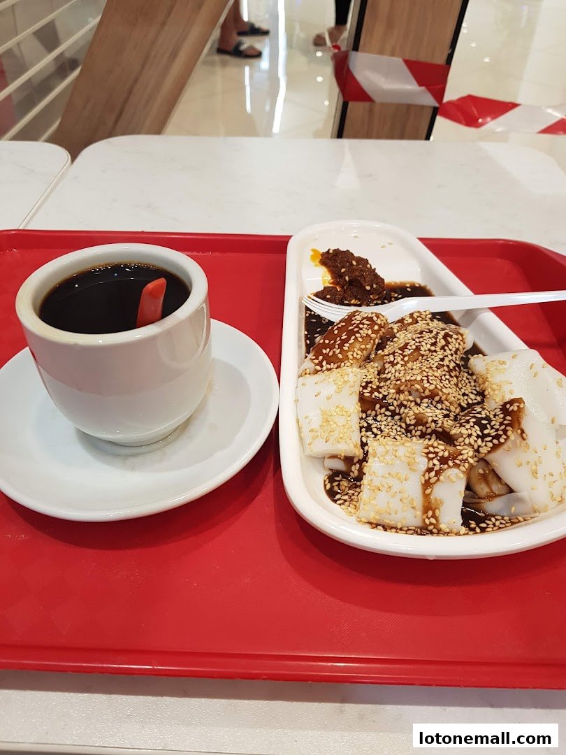 A red tray holds a cup of coffee and a plate of chee cheong fun with sesame seeds.