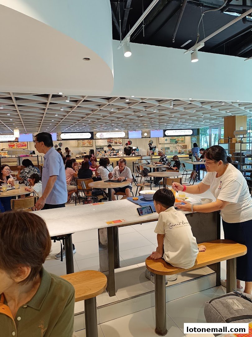 People dining and interacting at a busy food court with various food stalls visible.