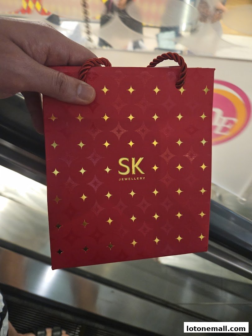 A hand holds a red SK Jewellery gift bag with gold star patterns.