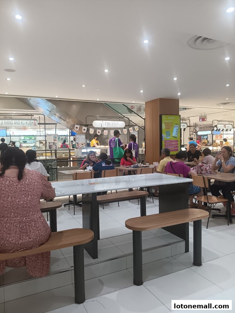 People dining at tables in a bright, modern food court with various food stalls visible.