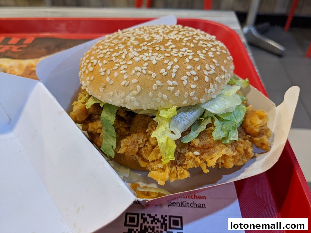 A close-up of a KFC chicken burger with lettuce in a white paper container.