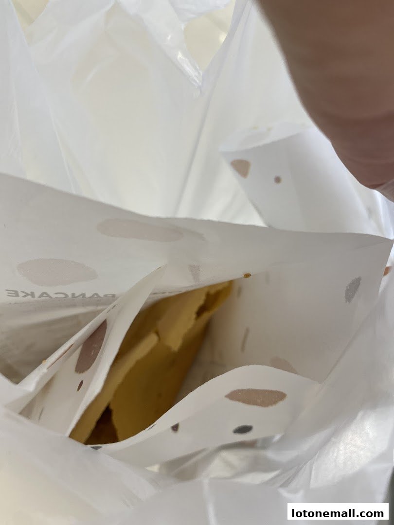 A close-up view inside a white paper bag with a pancake and branded paper.