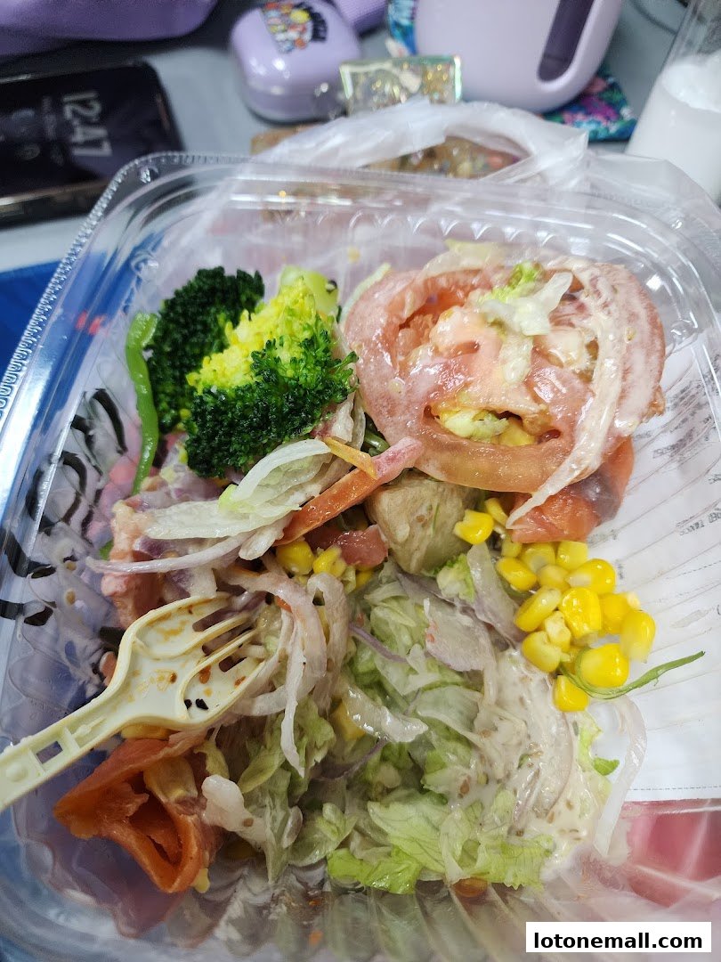 A close-up of a takeout salad with broccoli, tomatoes, corn, and other vegetables.