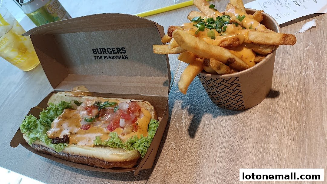 A hot dog and cheese fries are displayed on a wooden table, with a drink and receipt in the background.