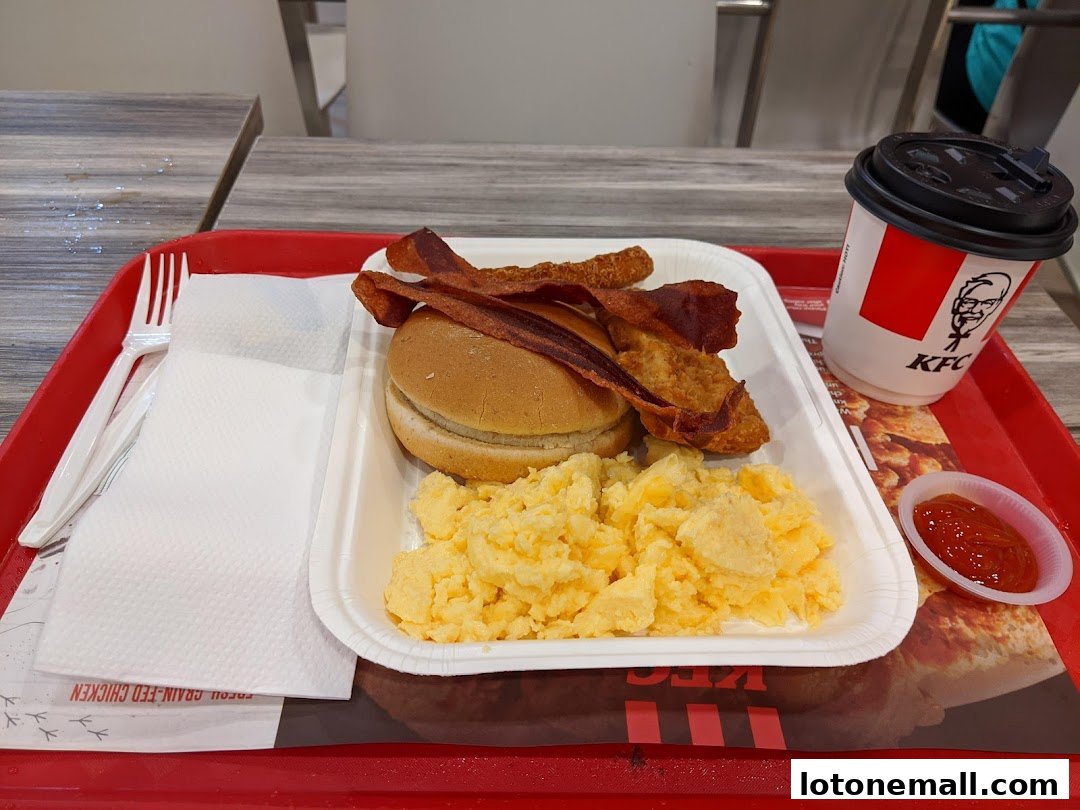 A KFC breakfast meal with scrambled eggs, a burger, bacon, and a drink.