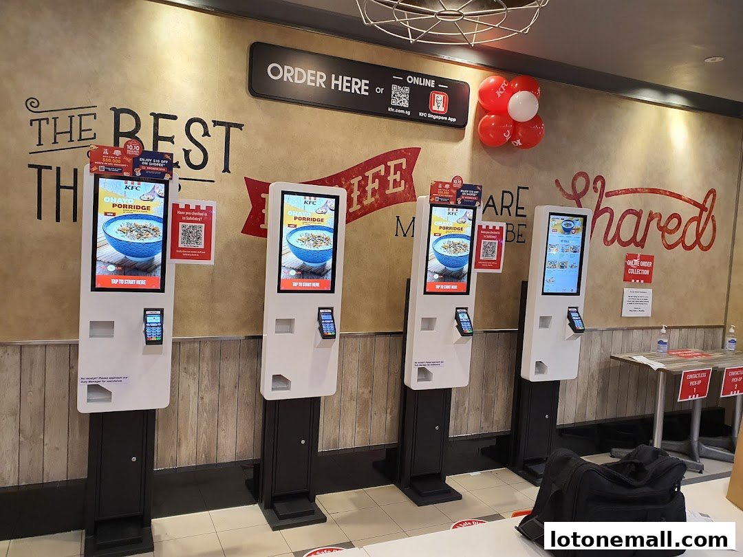 KFC restaurant with multiple self-order kiosks and a wall with promotional text.
