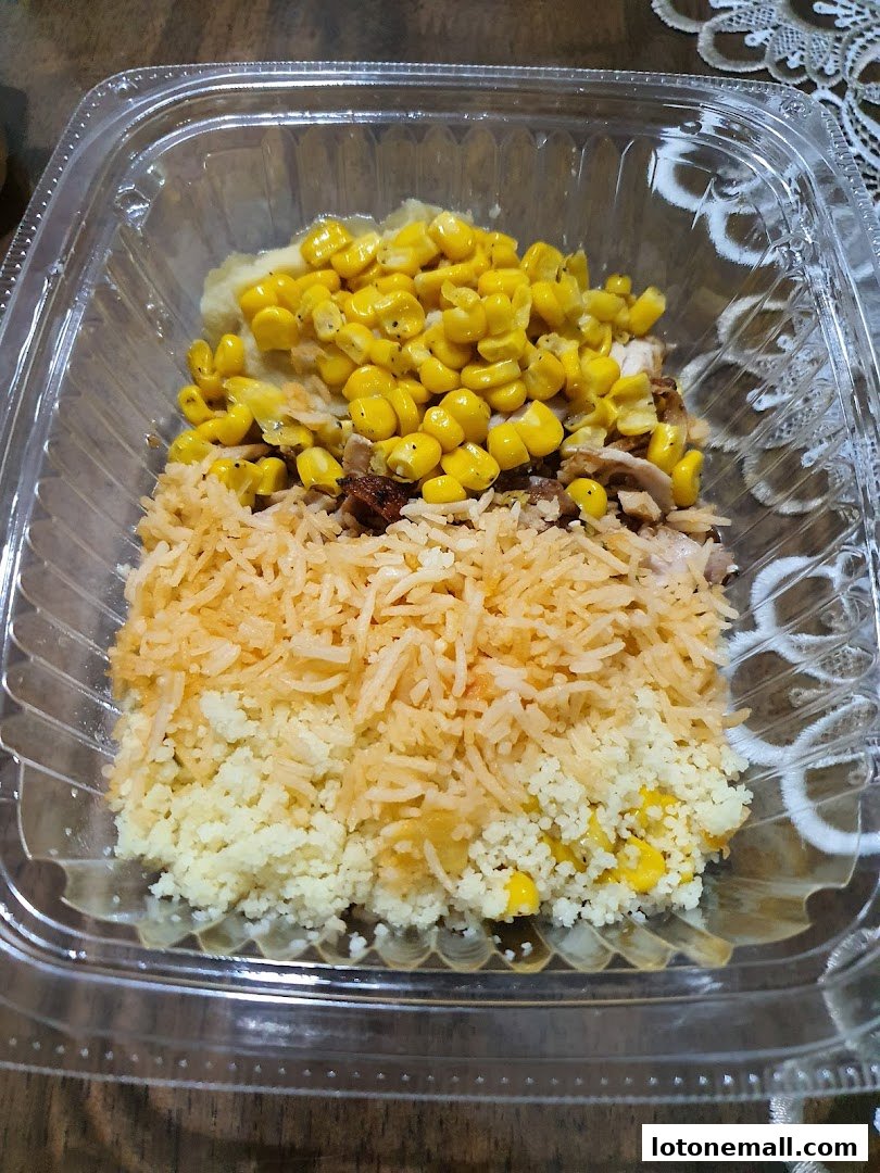 A clear plastic container filled with a meal of rice, corn, and mashed potatoes.