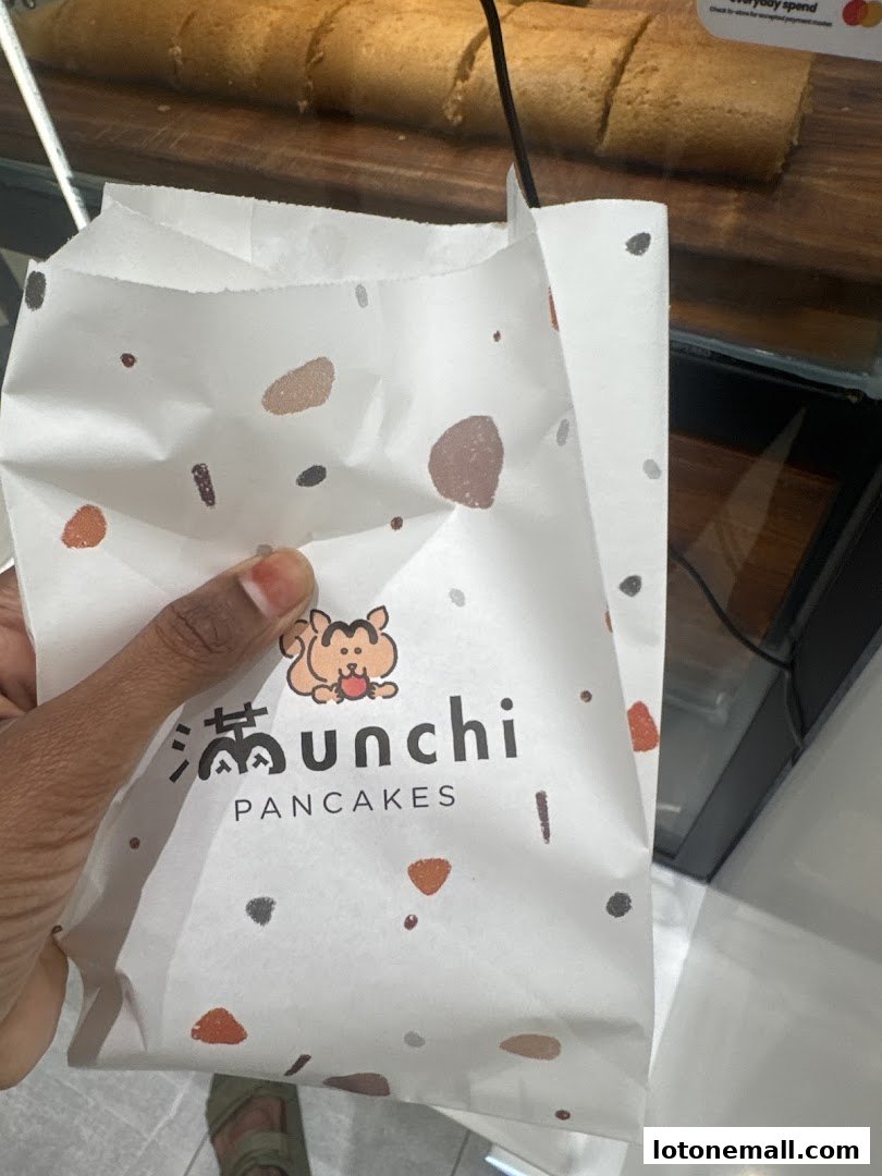A hand holds a paper bag with the Munchi Pancakes logo and a cartoon character.