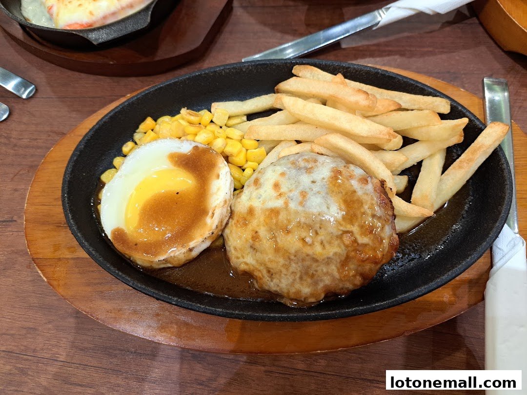 A sizzling hot plate meal featuring a hamburger steak, fried egg, french fries, and corn.