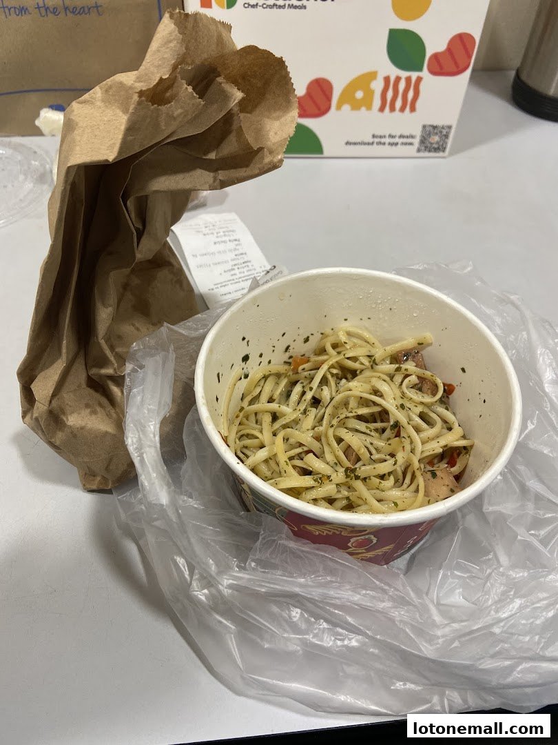 A bowl of pasta with a brown paper bag and a white box in the background.