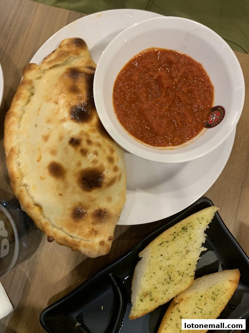 A calzone with marinara sauce and garlic bread on a wooden table.