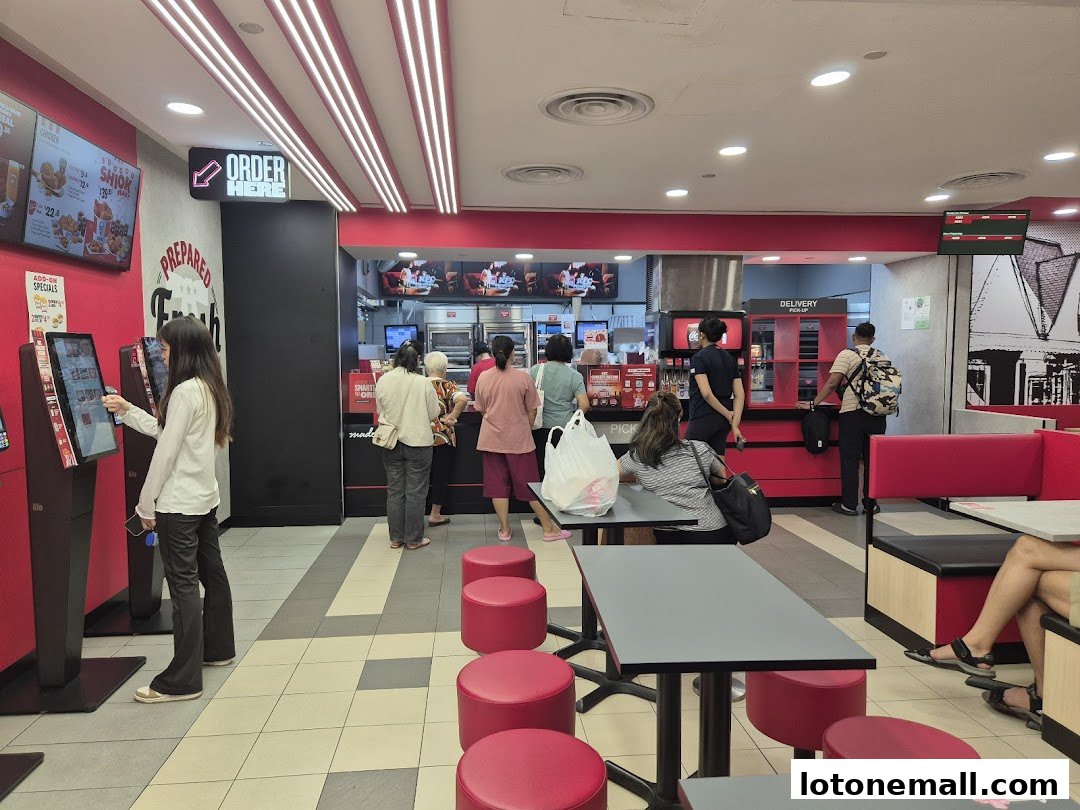 Customers ordering at self-service kiosks and waiting at the counter inside a KFC restaurant.