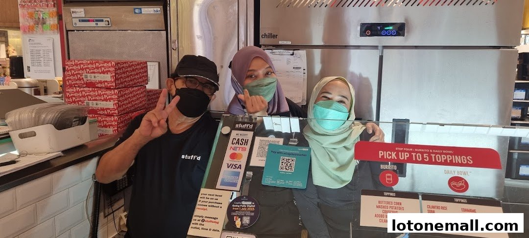 Three smiling staff members behind a counter at Stuff'd, a food establishment.