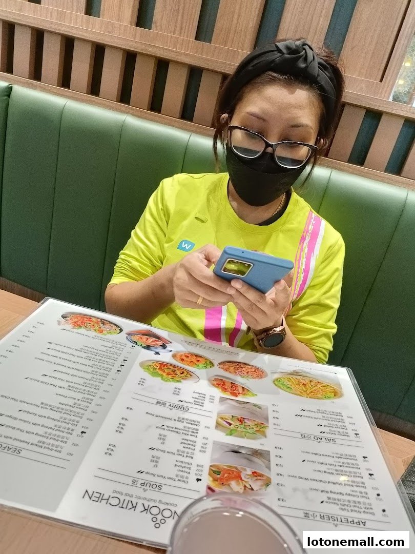 A person wearing a mask and glasses looks at a menu at Sanook Kitchen.
