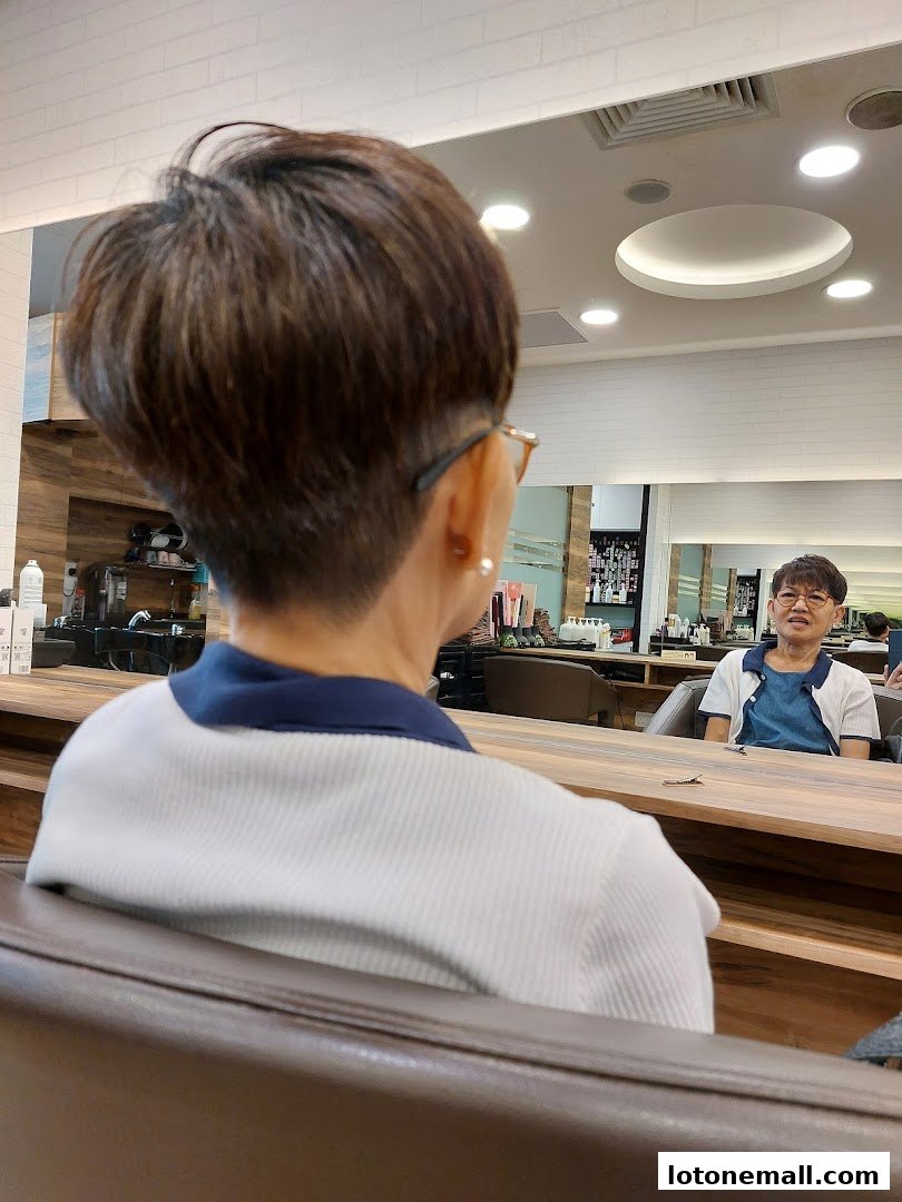 A person's back is shown as they sit in a salon chair, facing a mirror.