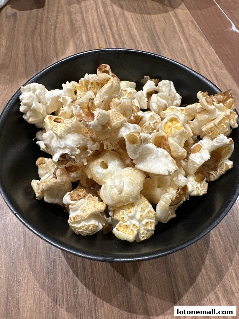 A black bowl filled with freshly popped popcorn on a wooden table.