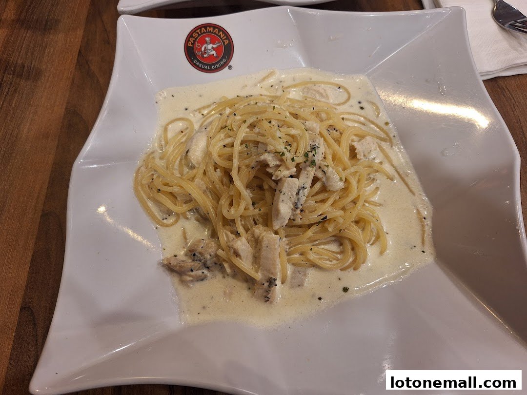 A plate of creamy chicken pasta with the PastaMania logo visible.