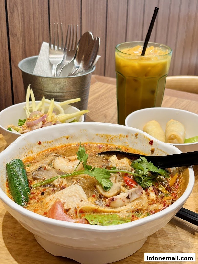 A close-up of a delicious Thai Tom Yum soup with a side of spring rolls and a refreshing drink.