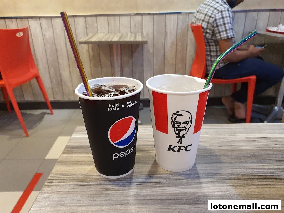 Two drinks with colorful straws on a table at KFC, with a person in the background.