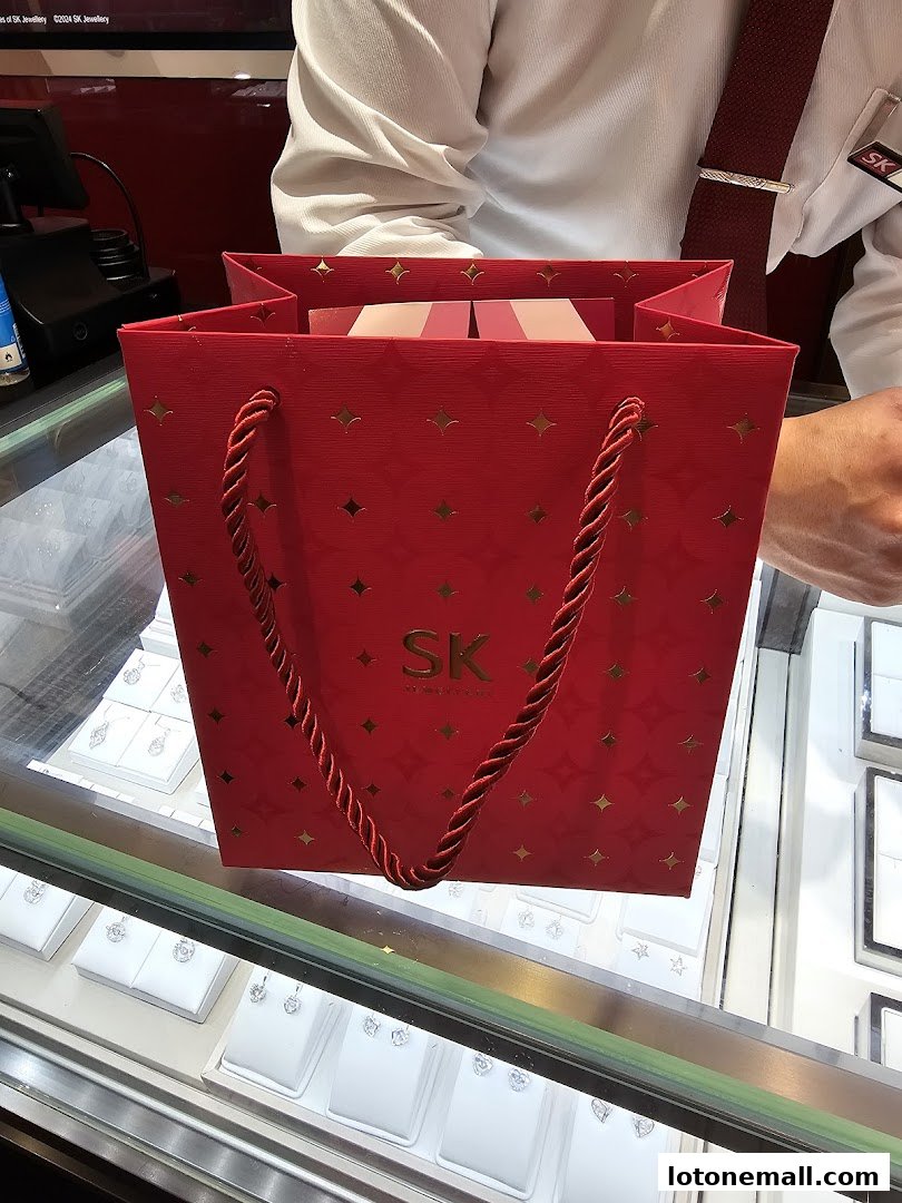 A red SK Jewellery shopping bag filled with gift boxes sits on a display case.