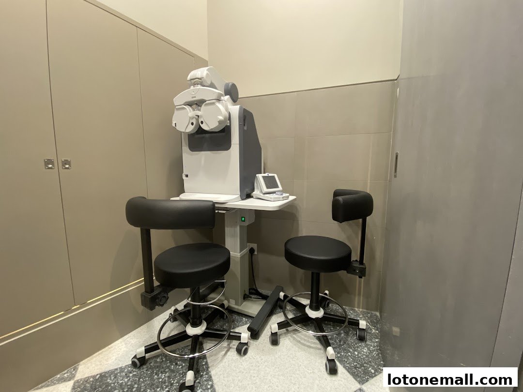 An eye examination room with a refractometer and two adjustable chairs.