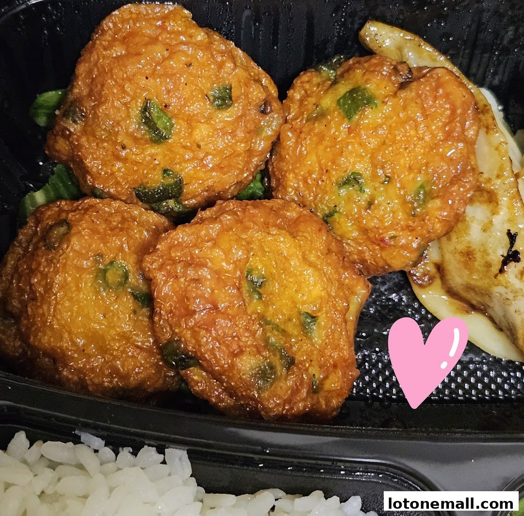 A close-up of a takeout container filled with golden-brown fried fish cakes, rice, and vegetables.