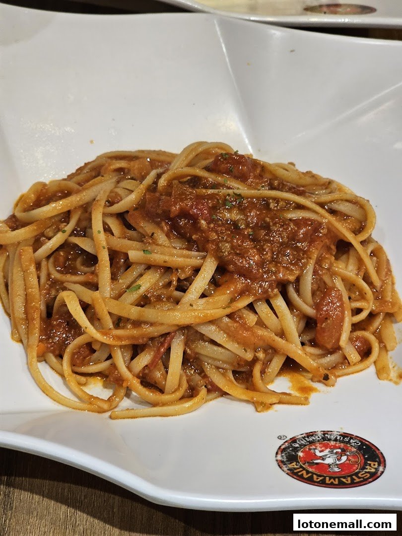 A plate of linguine pasta with a rich tomato meat sauce, garnished with herbs.