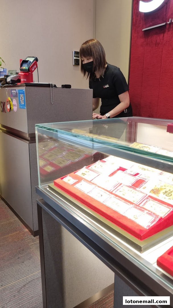 A staff member at the counter of SK Jewellery Lot One, with display cases of jewelry in the foreground.
