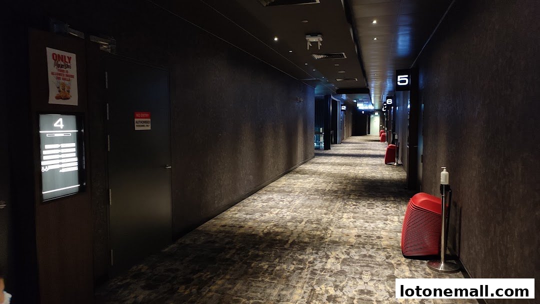 A dimly lit hallway in a cinema with numbered doors and red chairs stacked.