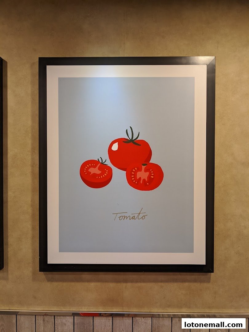 A framed picture of three red tomatoes, one whole and two halved, with the word 'Tomato' below.