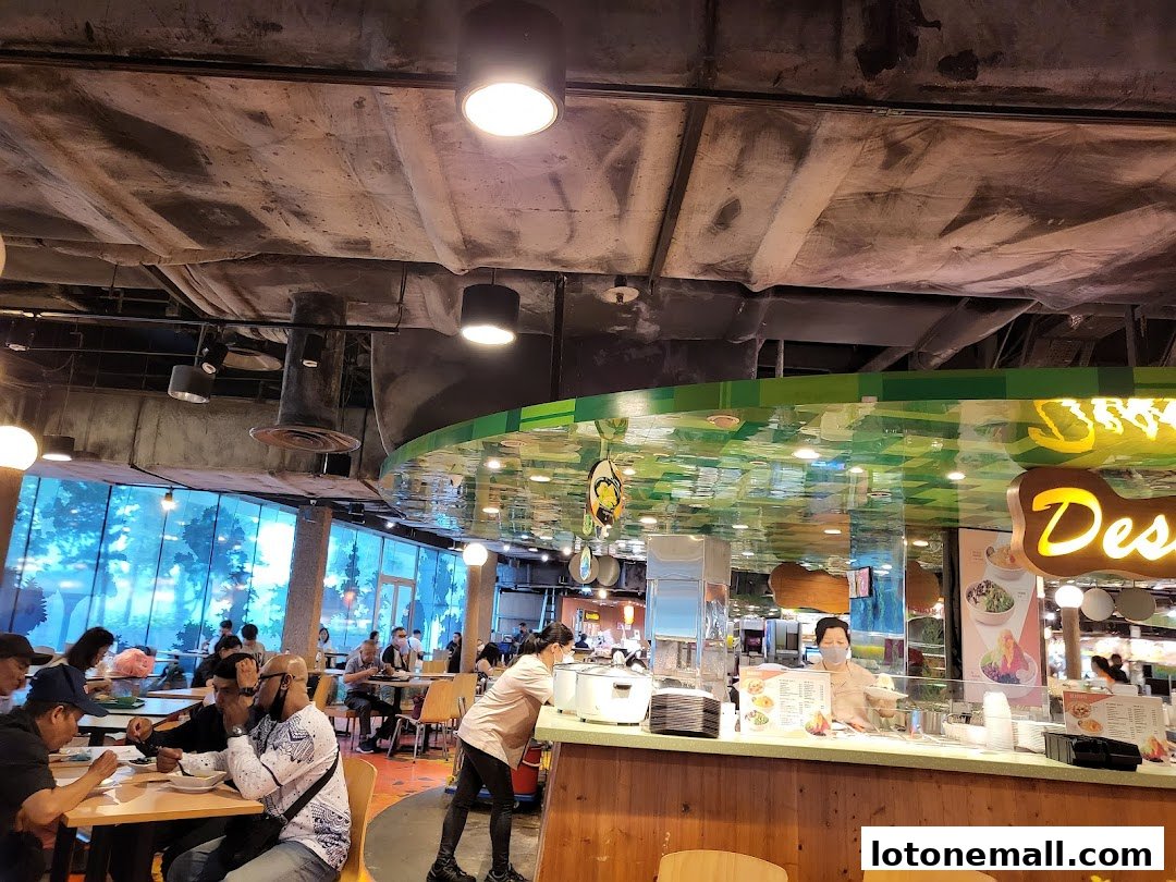 People dining at tables in a bustling food court with a dessert counter.